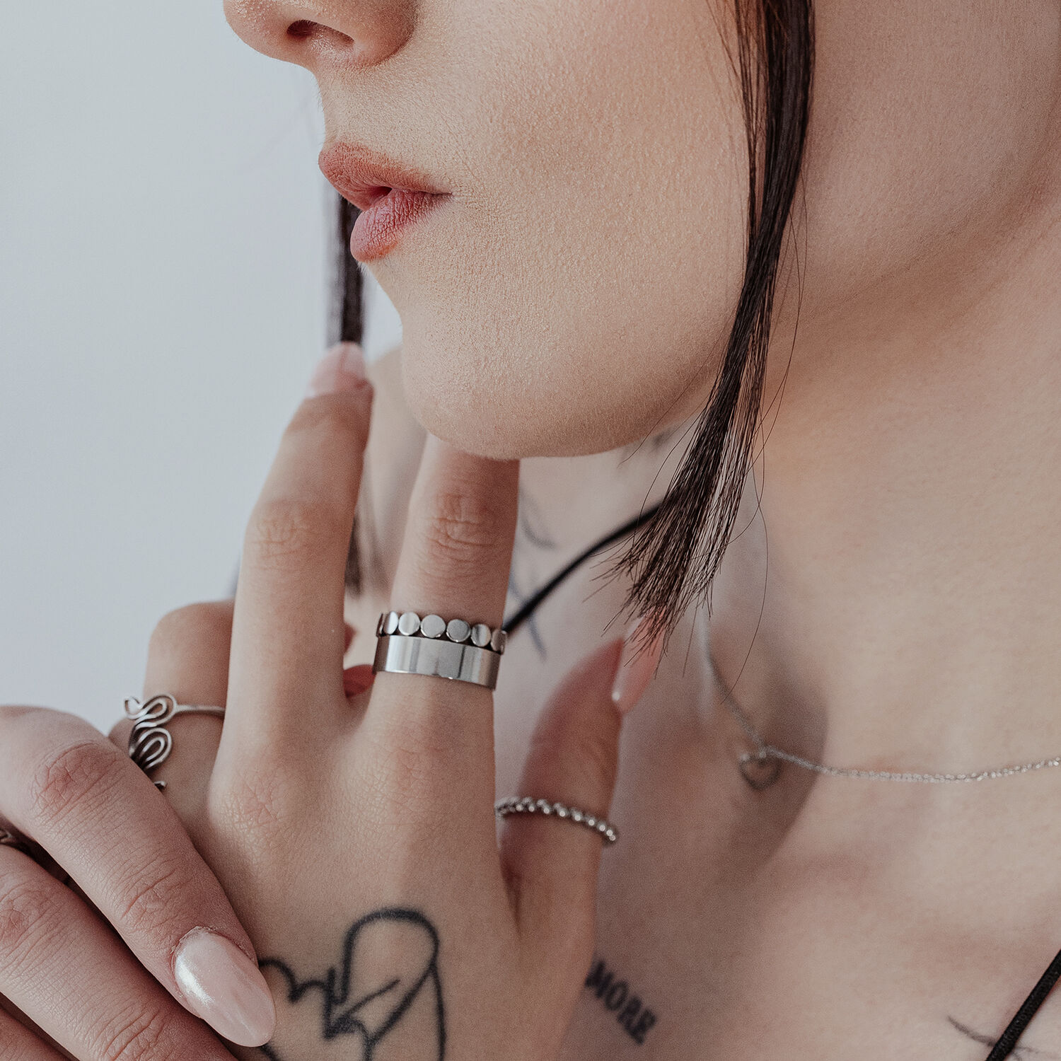 Bague à fines plaques en acier chirurgical argenté Gros plan d'une bague unisexe à fines plaques sur un doigt, argentée, peau tatouée en arrière-plan