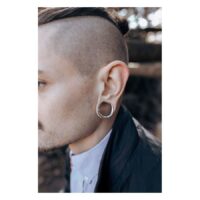 Homme avec des saddles d'oreilles argentées dans l'oreille devant un fond flou