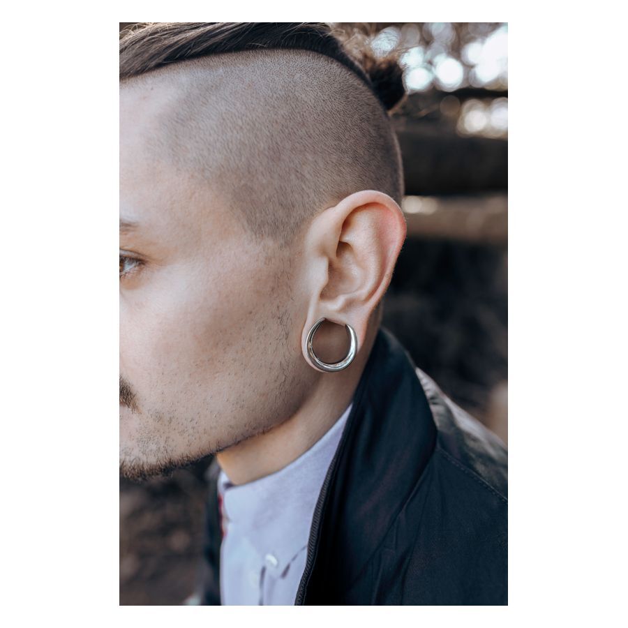 Homme avec des saddles d'oreilles argentées dans l'oreille devant un fond flou