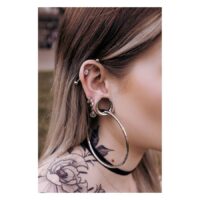 Saddles d'oreille argentés et noirs sur une oreille avec piercings, tatouage en arrière-plan