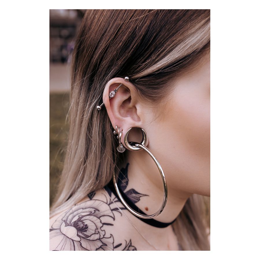 Saddles d'oreille argentés et noirs sur une oreille avec piercings, tatouage en arrière-plan