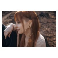 Stylische ovale Ear Saddles in Gold Femme avec des Ear Saddles ovales en or dans l'oreille, à l'extérieur au soleil