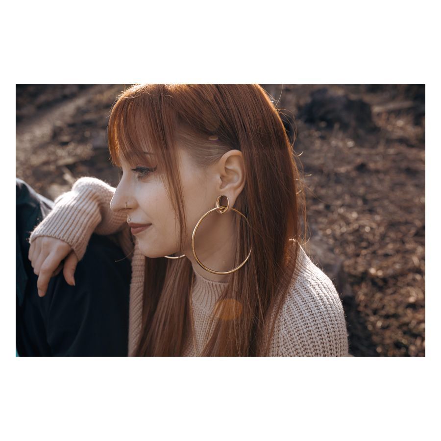 Stylische ovale Ear Saddles in Gold Femme avec des Ear Saddles ovales en or dans l'oreille, à l'extérieur au soleil