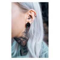 Gros plan d'une oreille avec des saddles d'oreille Monstera noires et d'autres piercings, arrière-plan flou