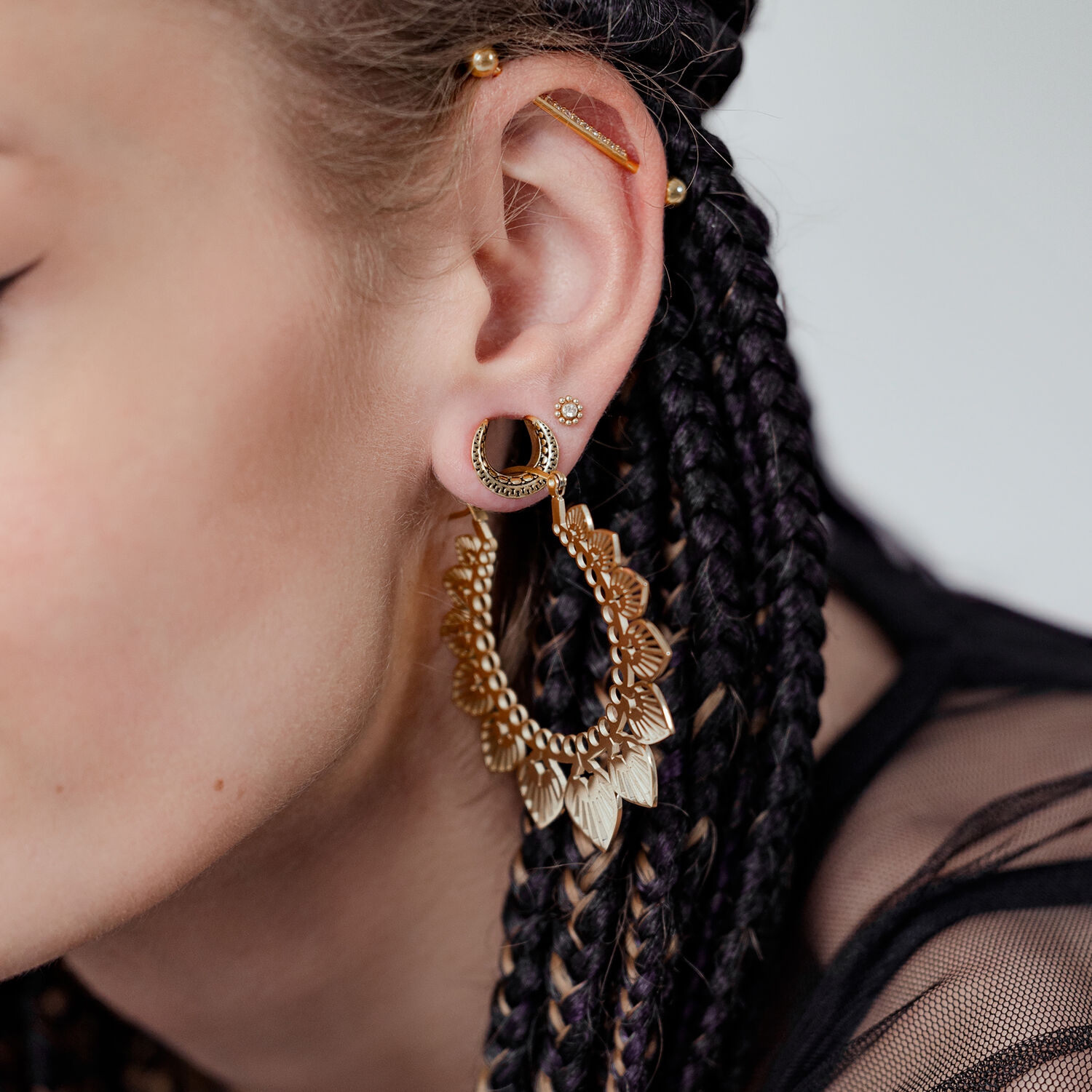 Ear Saddles Maori dorées dans l'oreille Gros plan d'une oreille avec des cheveux tressés portant des Ear Saddles Maori dorées