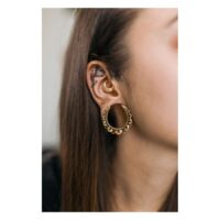 Boucles d'oreilles fleurs en or portées à l'oreille Boucles d'oreilles fleurs en or dans l'oreille avec d'autres piercings sur fond neutre