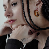 Twisted poids d'oreille en or portés à l'oreille Femme avec des poids d'oreille Twisted en or et des tresses sur fond gris