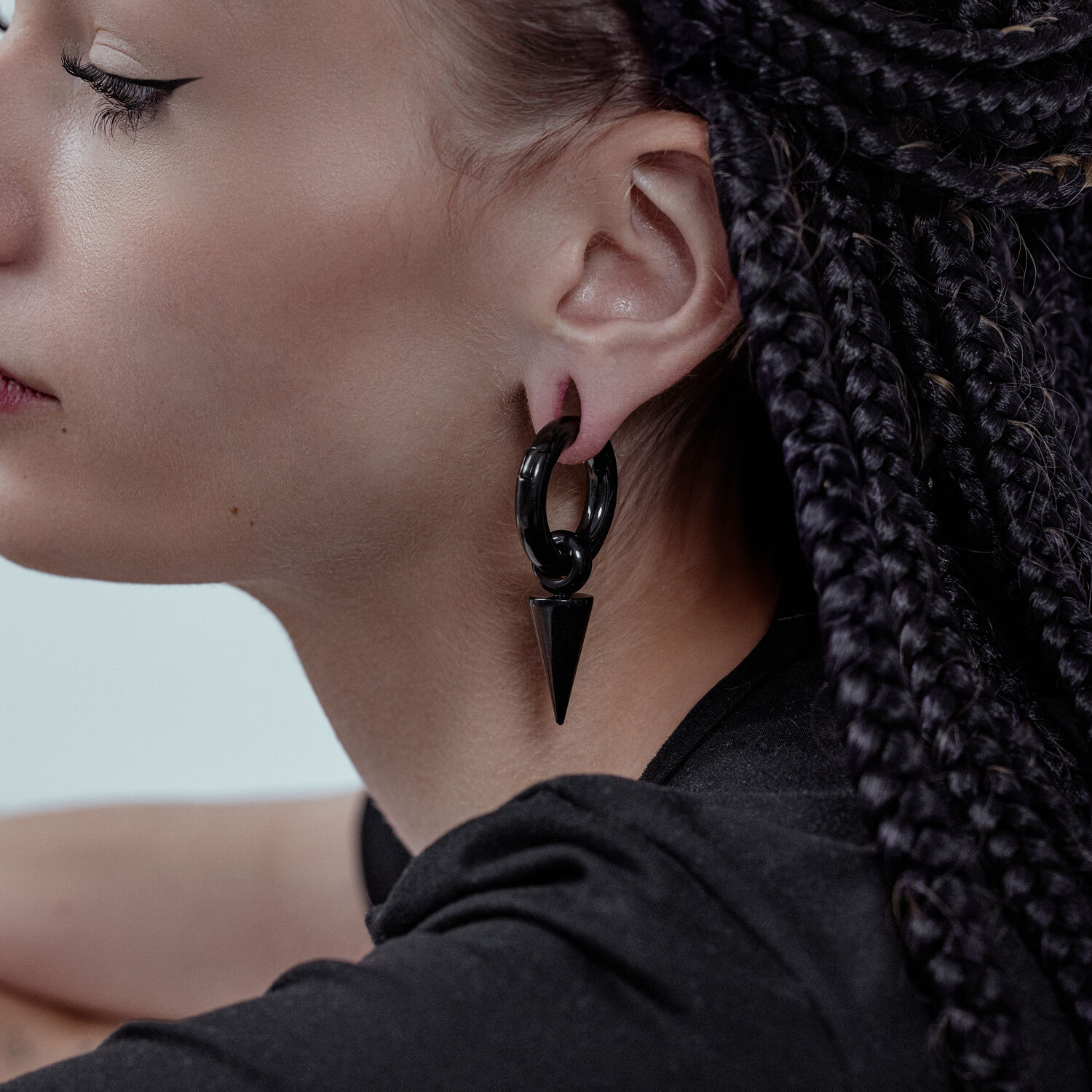 Flèches noires portées dans l'oreille Gros plan d'une personne avec des flèches noires en acier chirurgical, cheveux tressés en arrière-plan