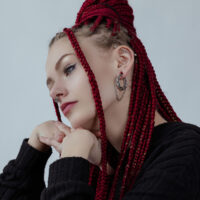 Wildcat Double Chain Poids d'Oreille en Argent Femme aux tresses rouges portant des poids d'oreille Double Chain en argent et un pull noir sur fond gris