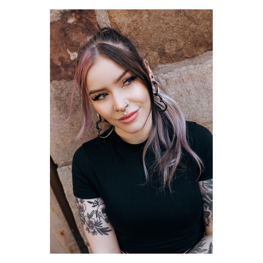 Labret Push-Fit Oriental Sun dans l'oreille Femme avec boucles d'oreilles et piercings noirs et argentés, souriante devant un mur de pierre