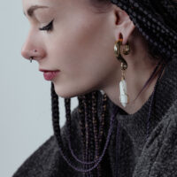 Poids d'oreilles en pierre Opilate dorés à l'oreille Femme aux cheveux tressés portant des poids d'oreilles dorés avec des pierres blanches.