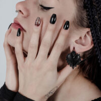 Poids d'oreille Sacred Heart noirs dans l'oreille Femme avec des poids d'oreille Sacred Heart noirs et vernis à ongles noir, vue de côté