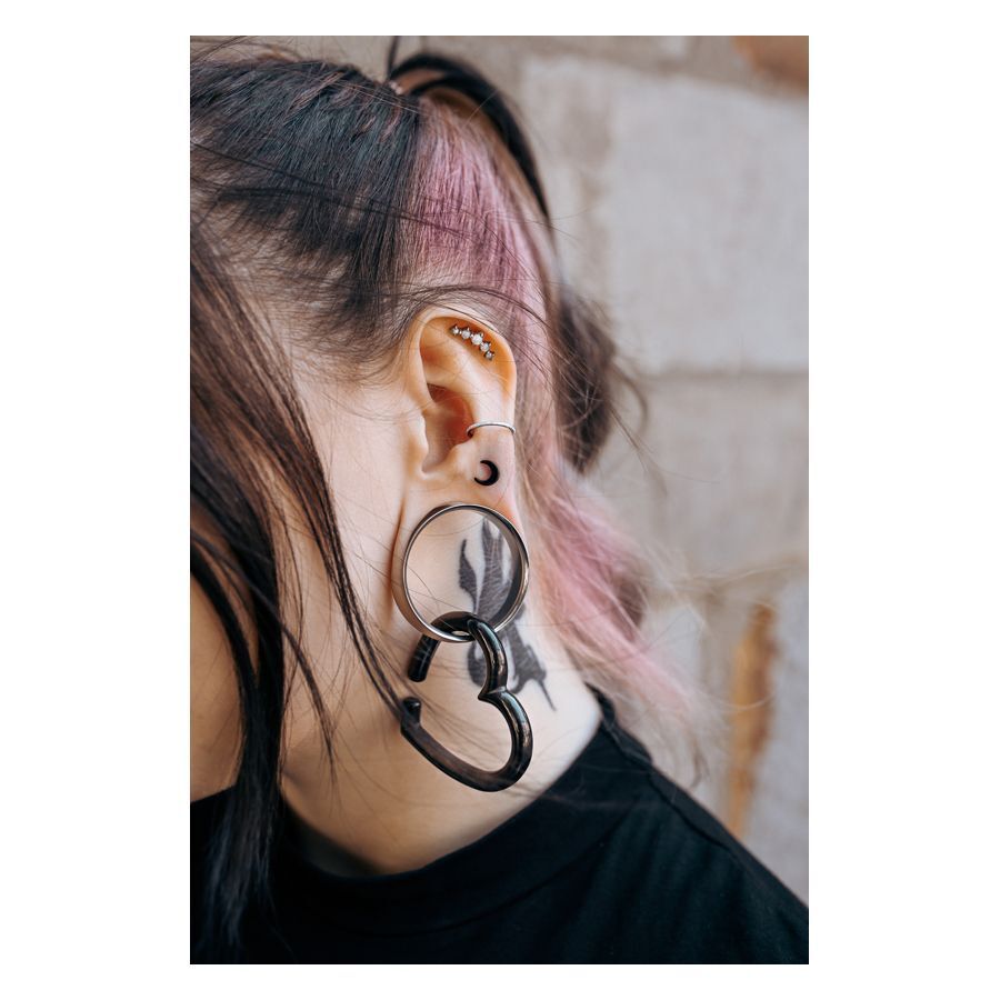 Luna Earbarbell en noir et argent Oreille avec plusieurs piercings, y compris un Luna Earbarbell noir et un grand tunnel, mèche de cheveux rose