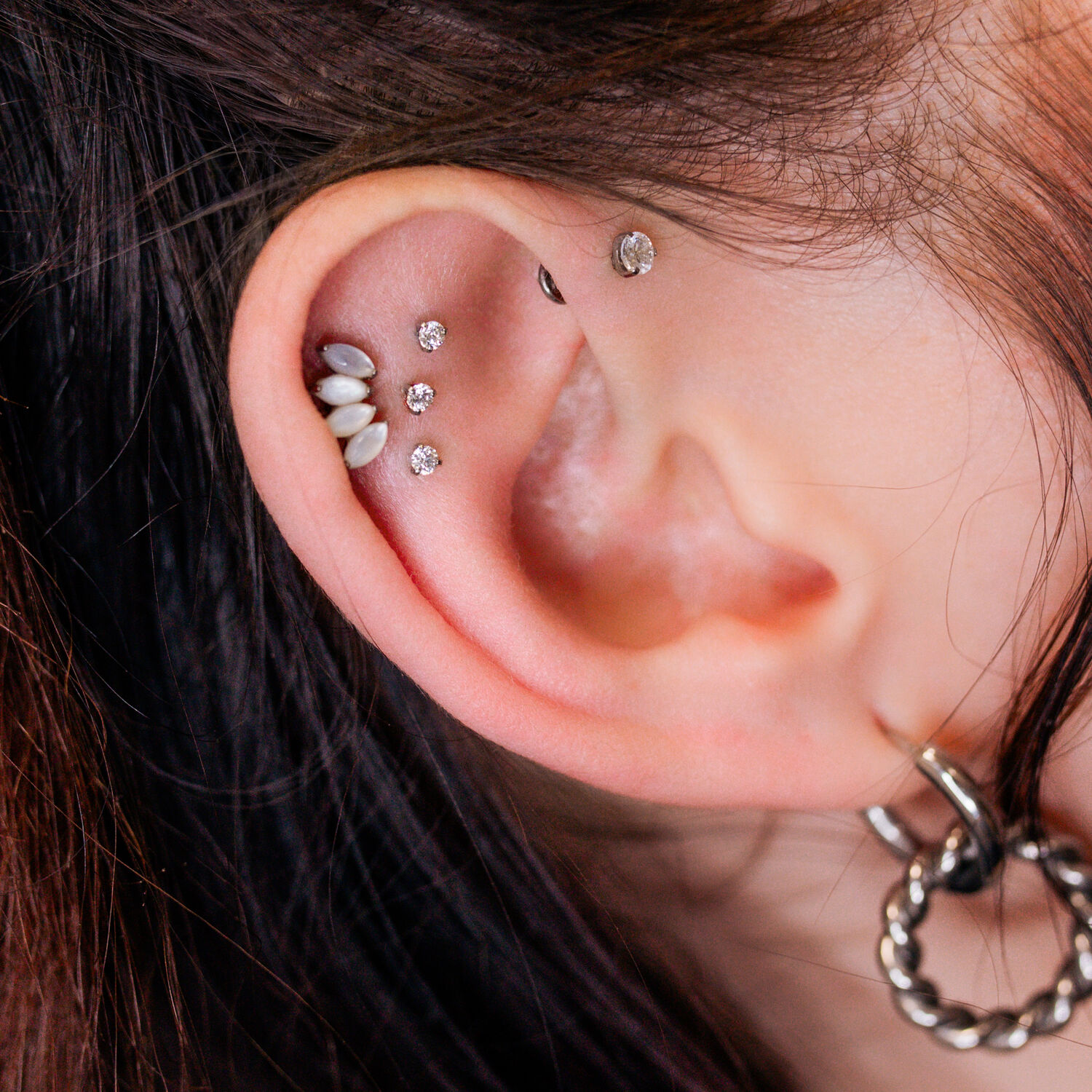 Piercing d'oreille avec Triple Labret Pushfit Gros plan d'une oreille avec plusieurs piercings scintillants, y compris un Triple Labret Pushfit, sur fond clair