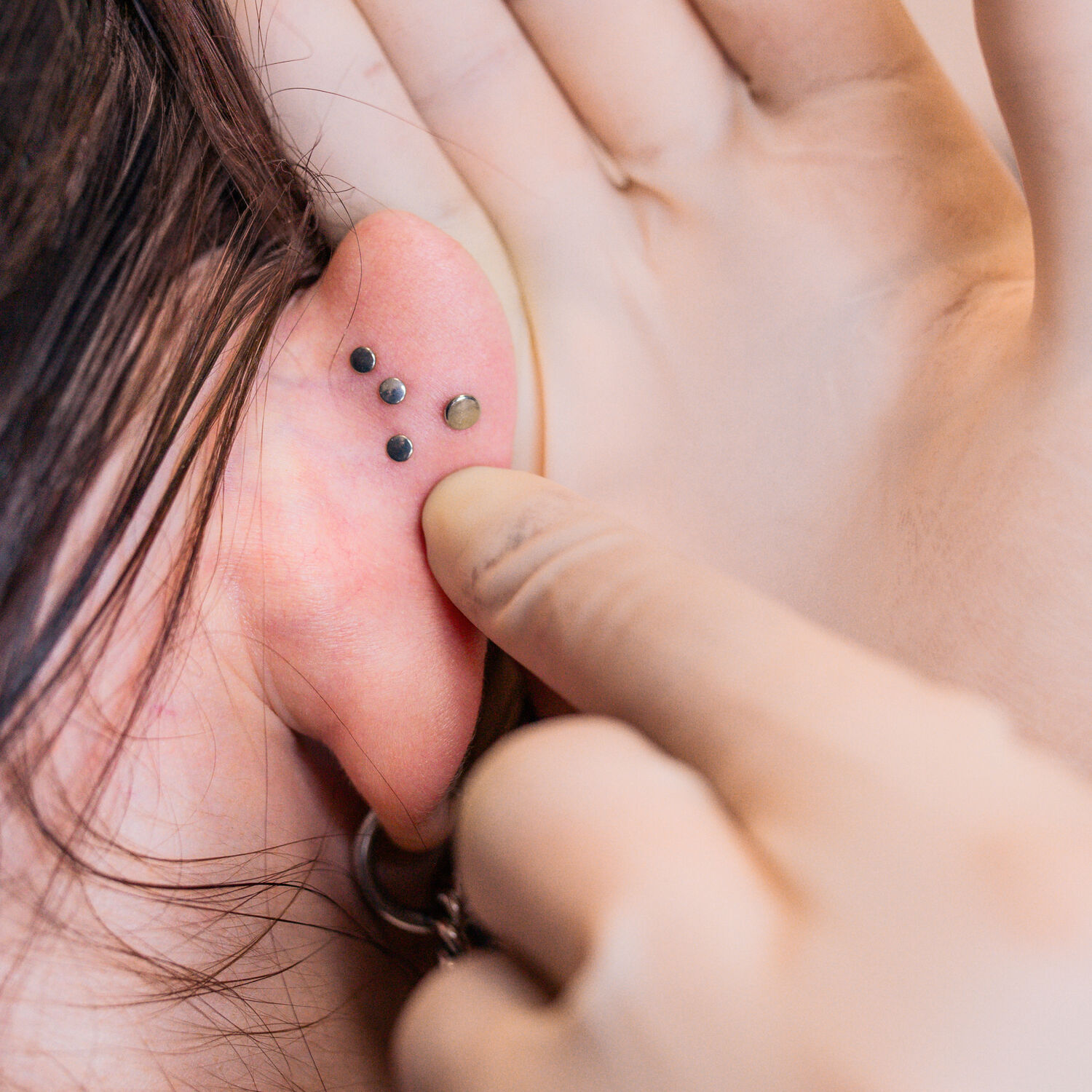 Labret Piercing avec Design Triple Pushfit Gros plan d'une oreille avec trois piercings Labret noirs et un doigt touchant les piercings.