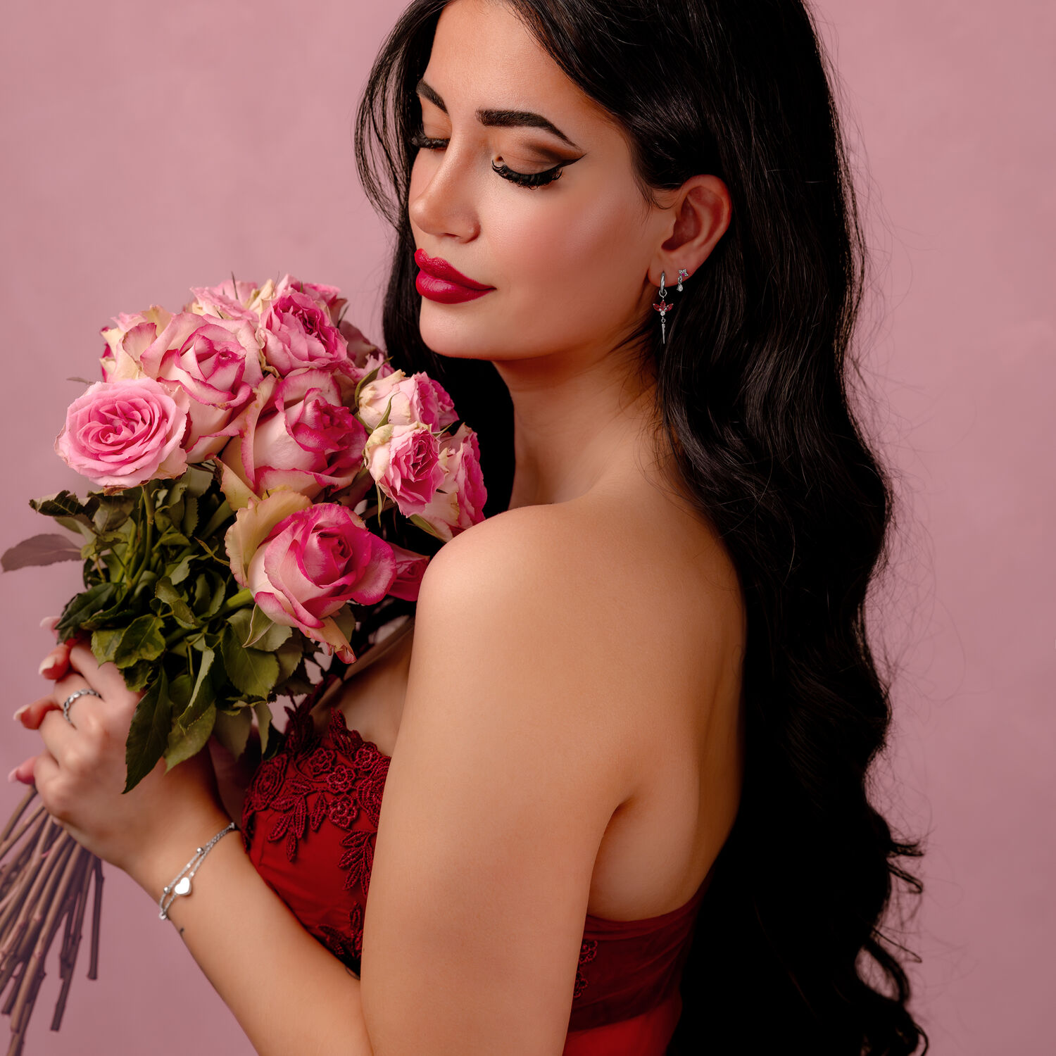 Femme avec un bouquet de roses en robe rouge Femme aux longs cheveux bruns tenant un bouquet de roses roses sur fond rose.