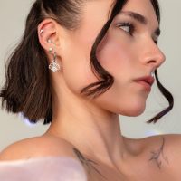 Femme avec plusieurs piercings d'oreilles en argent, y compris un pendentif chaîne, sur fond neutre