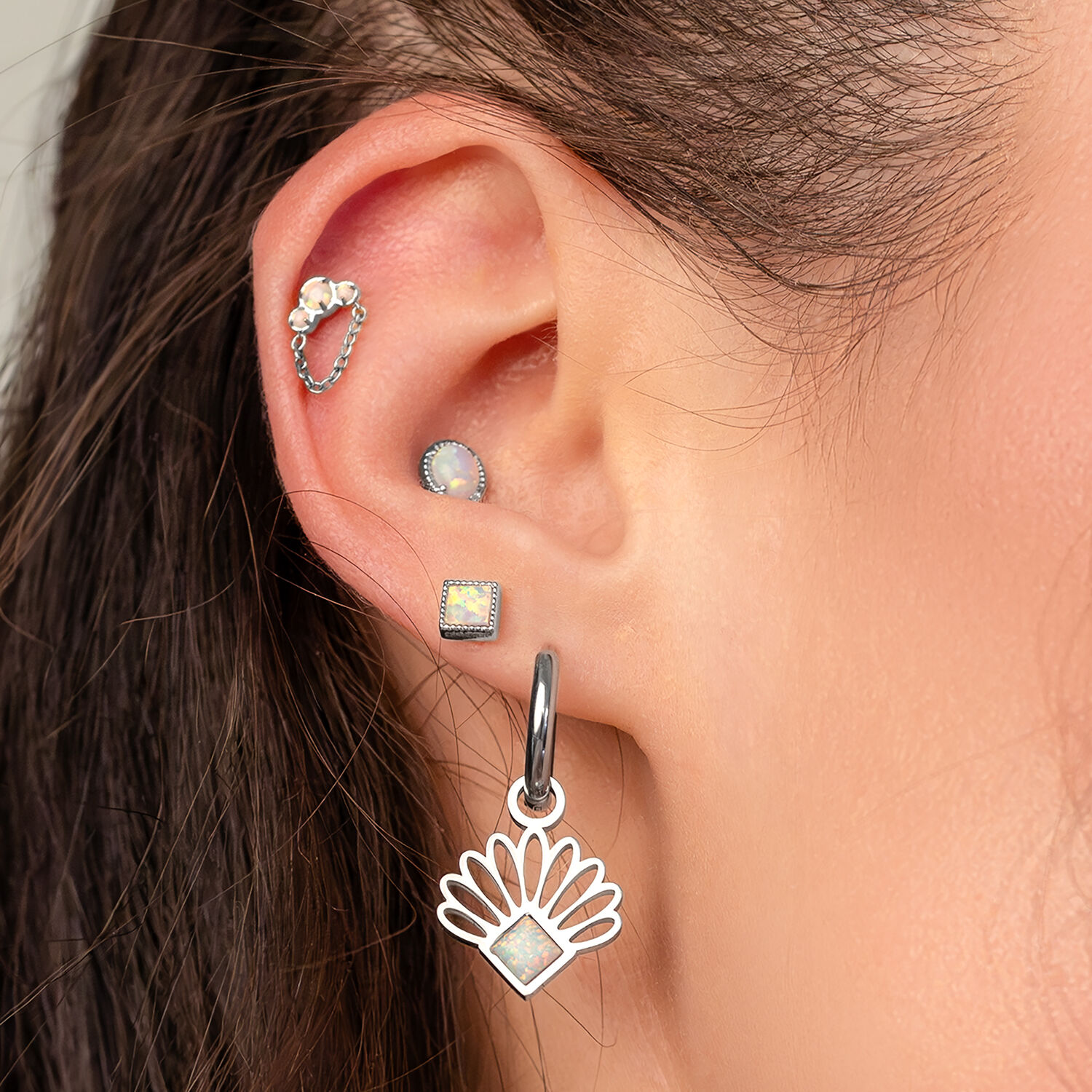 Gros plan d'une oreille avec plusieurs piercings, dont un piercing en opale avec chaîne