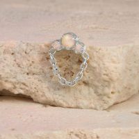 Piercing en or blanc avec opale et chaîne sur une pierre beige