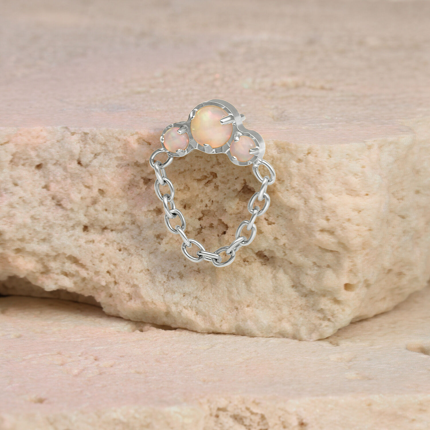 Piercing en or blanc avec opale et chaîne sur une pierre beige