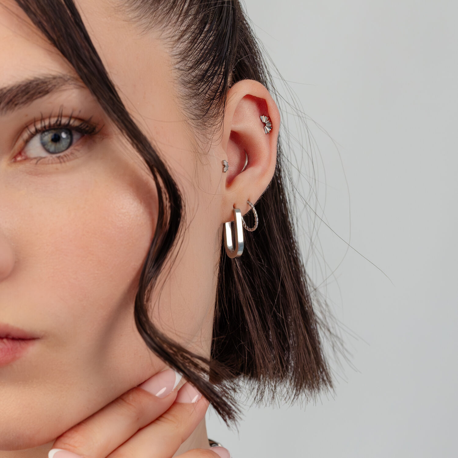 Créoles en argent et piercing d'oreille Gros plan d'une oreille avec des créoles en argent et plusieurs piercings d'oreille sur fond gris.
