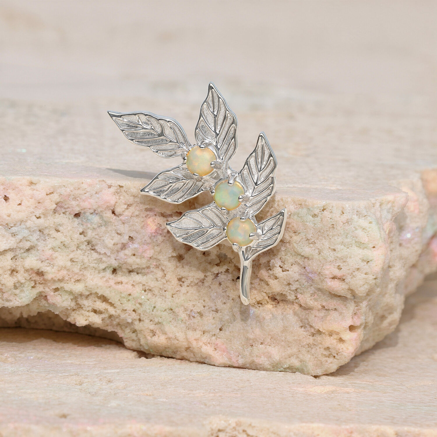 Pendentif en forme de feuille avec des pierres d'opale sur une pierre beige