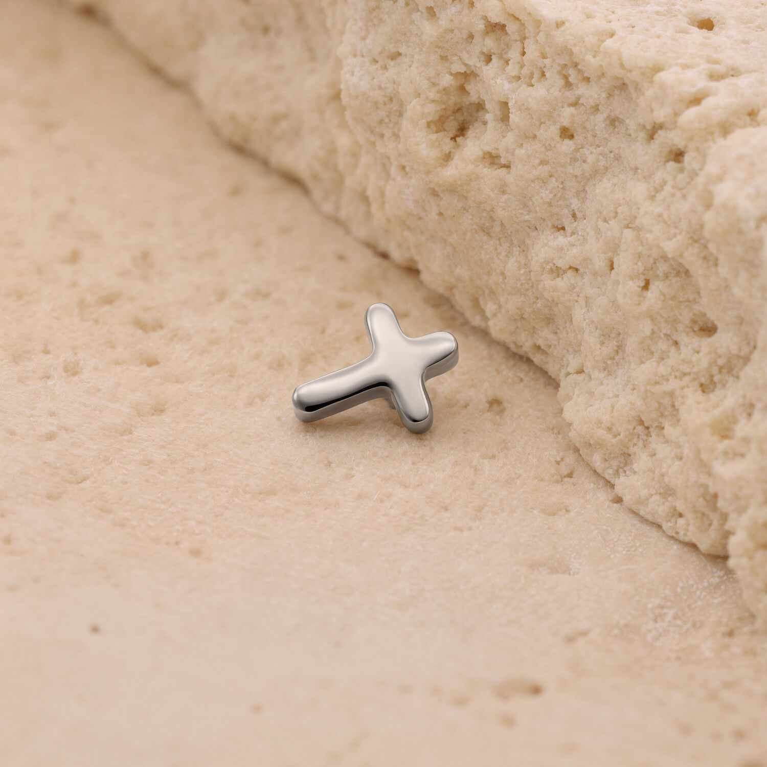 Embout croix en titane argenté sur fond sablonneux
