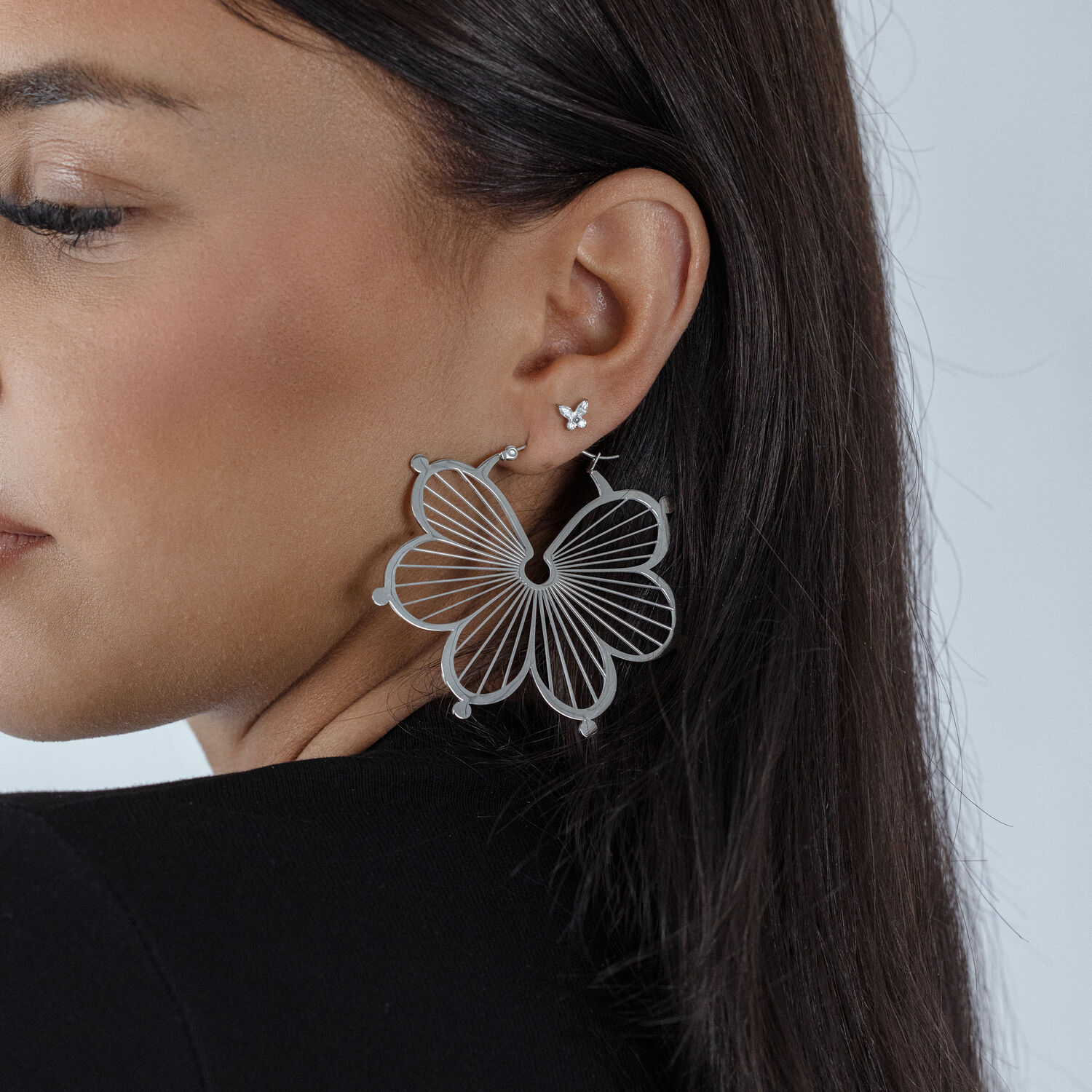 Femme avec un grand embout papillon argenté dans l'oreille, fond noir