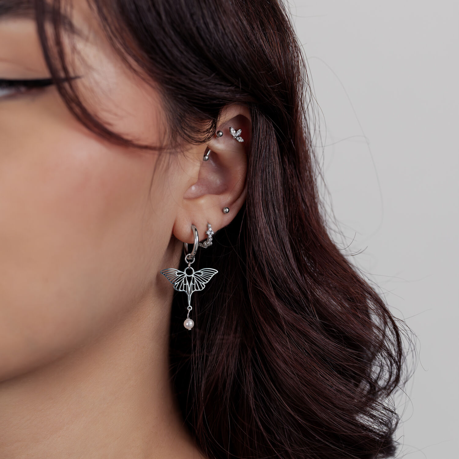 Piercings d'oreilles argentés avec pendentif papillon Femme avec plusieurs piercings d'oreilles argentés et un pendentif papillon sur fond clair