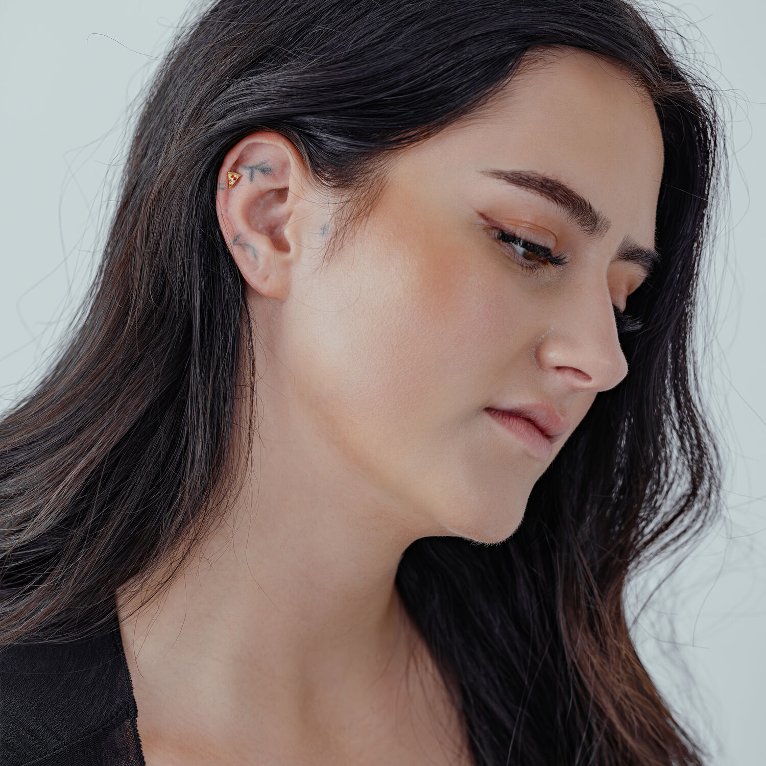 Femme aux longs cheveux noirs portant une pizza dorée à l'oreille sur fond clair