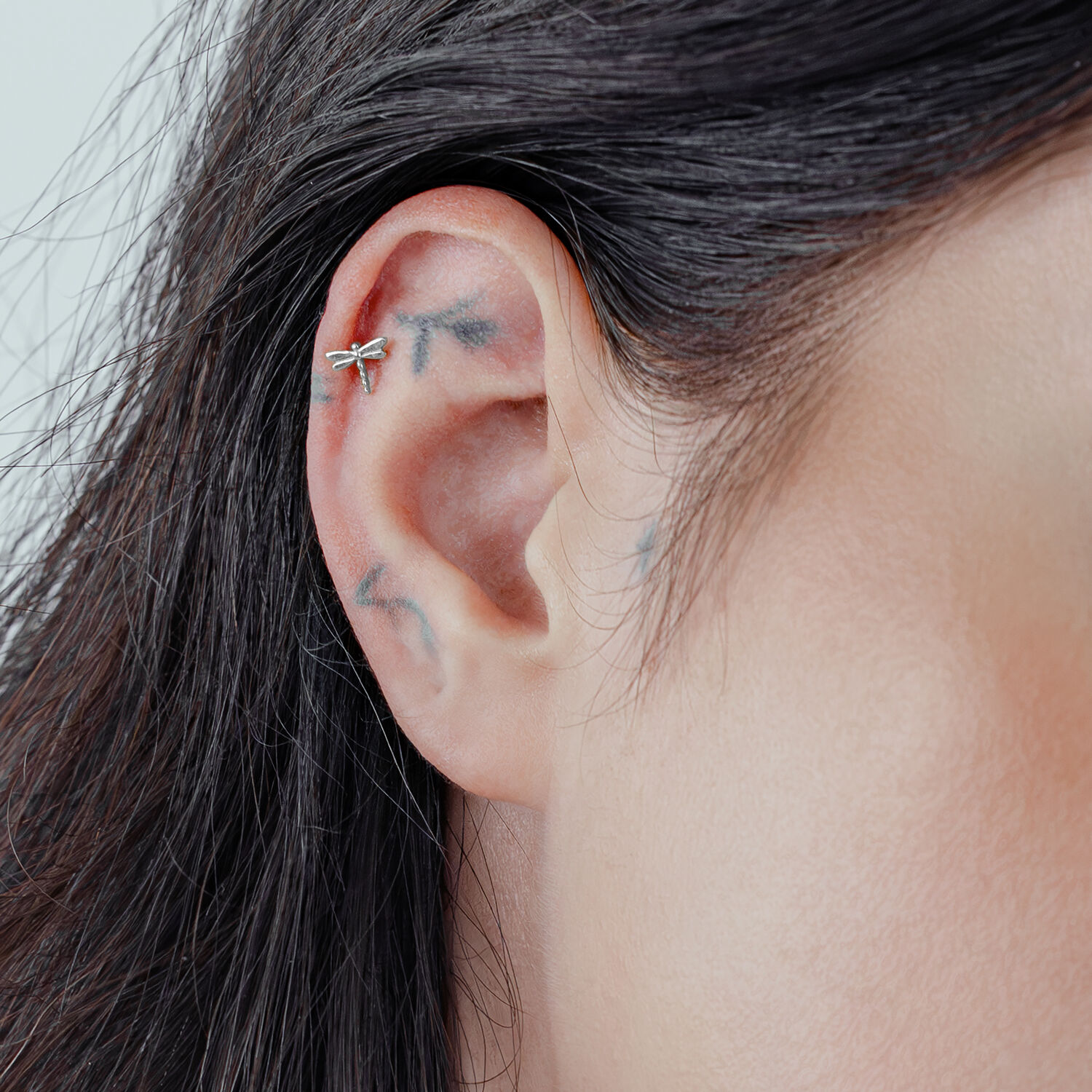 Embout de libellule en argent sur un piercing d'oreille sur fond clair