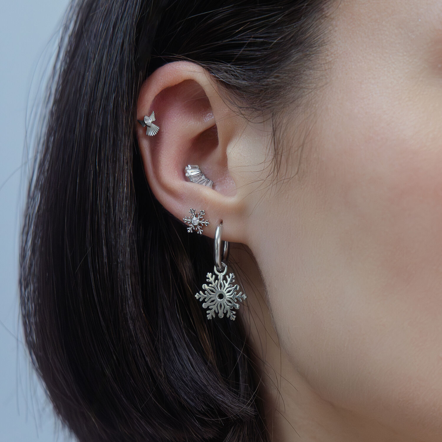 Embout de piercing flocon de neige argenté Oreille avec plusieurs piercings argentés, design flocon de neige, sur fond neutre