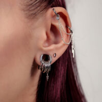 Gros plan d'une oreille avec embouts de piercing argentés et chaînes