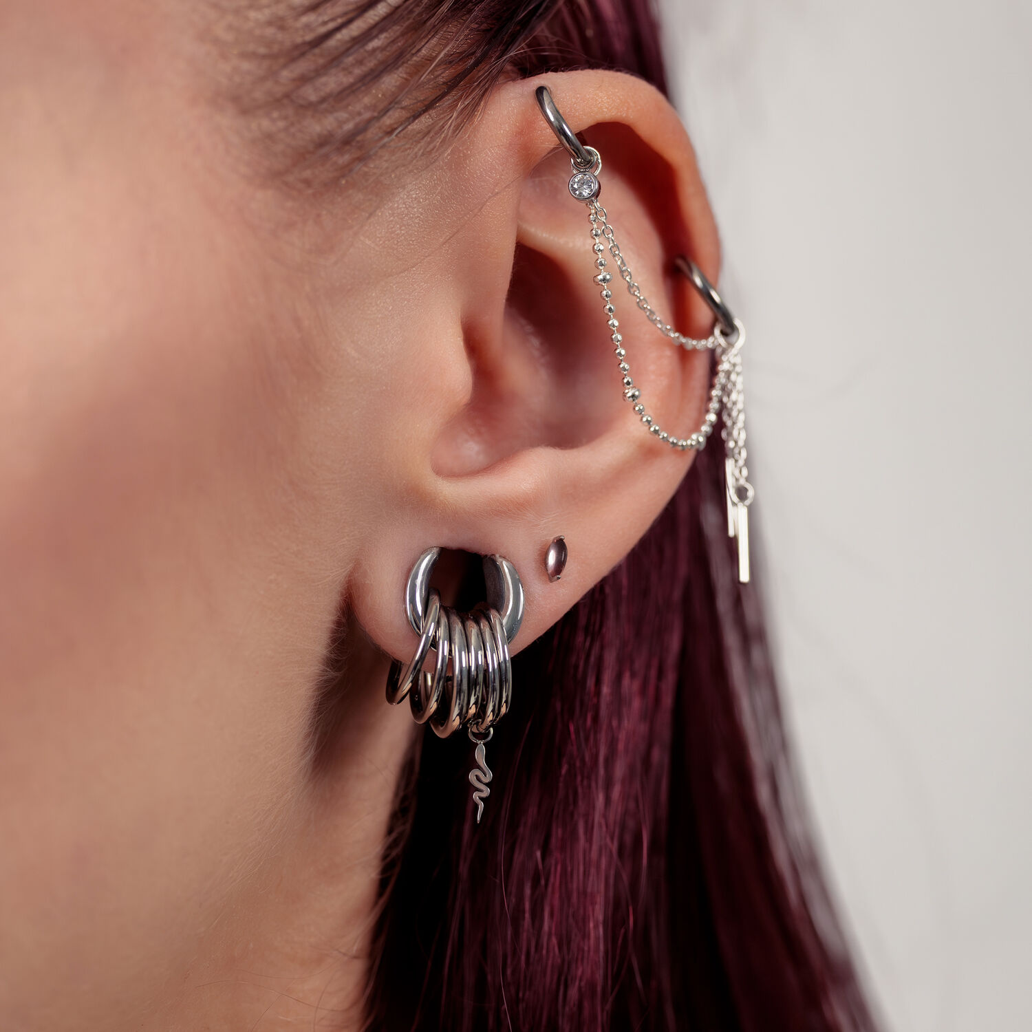 Gros plan d'une oreille avec embouts de piercing argentés et chaînes