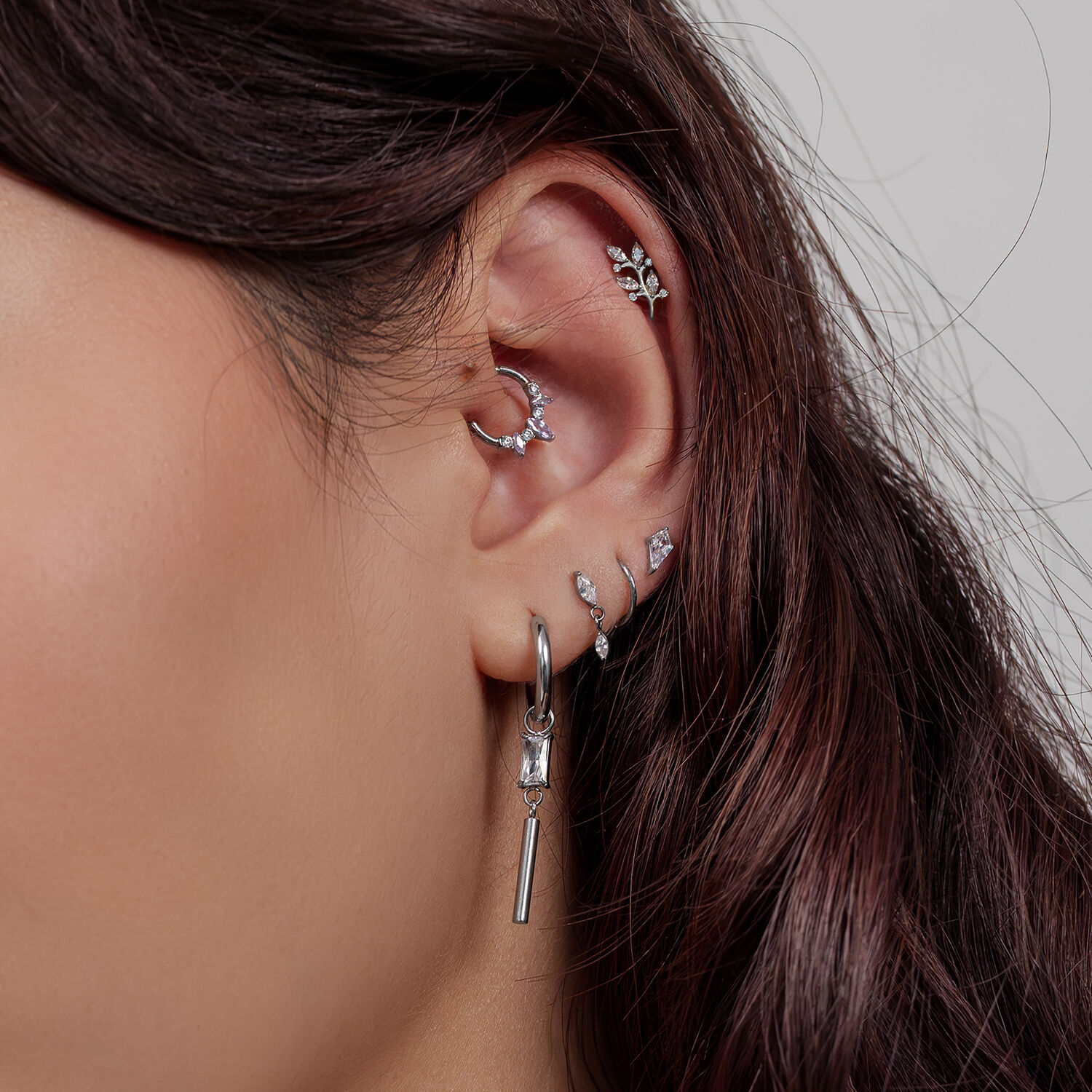 Oreille avec plusieurs piercings argentés, y compris des designs de feuille de cristal, sur fond clair