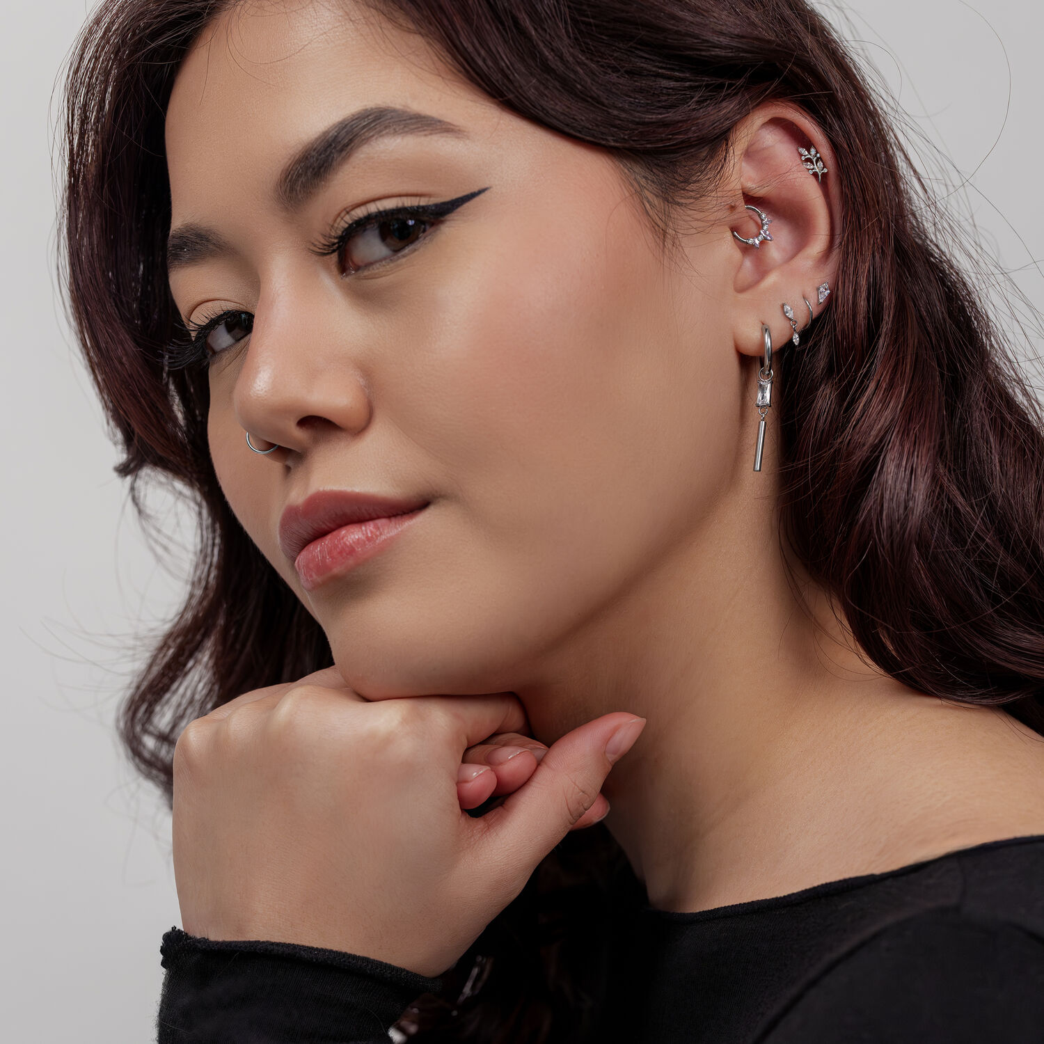 Femme avec des piercings d'oreille argentés, y compris une feuille de cristal, sur fond gris