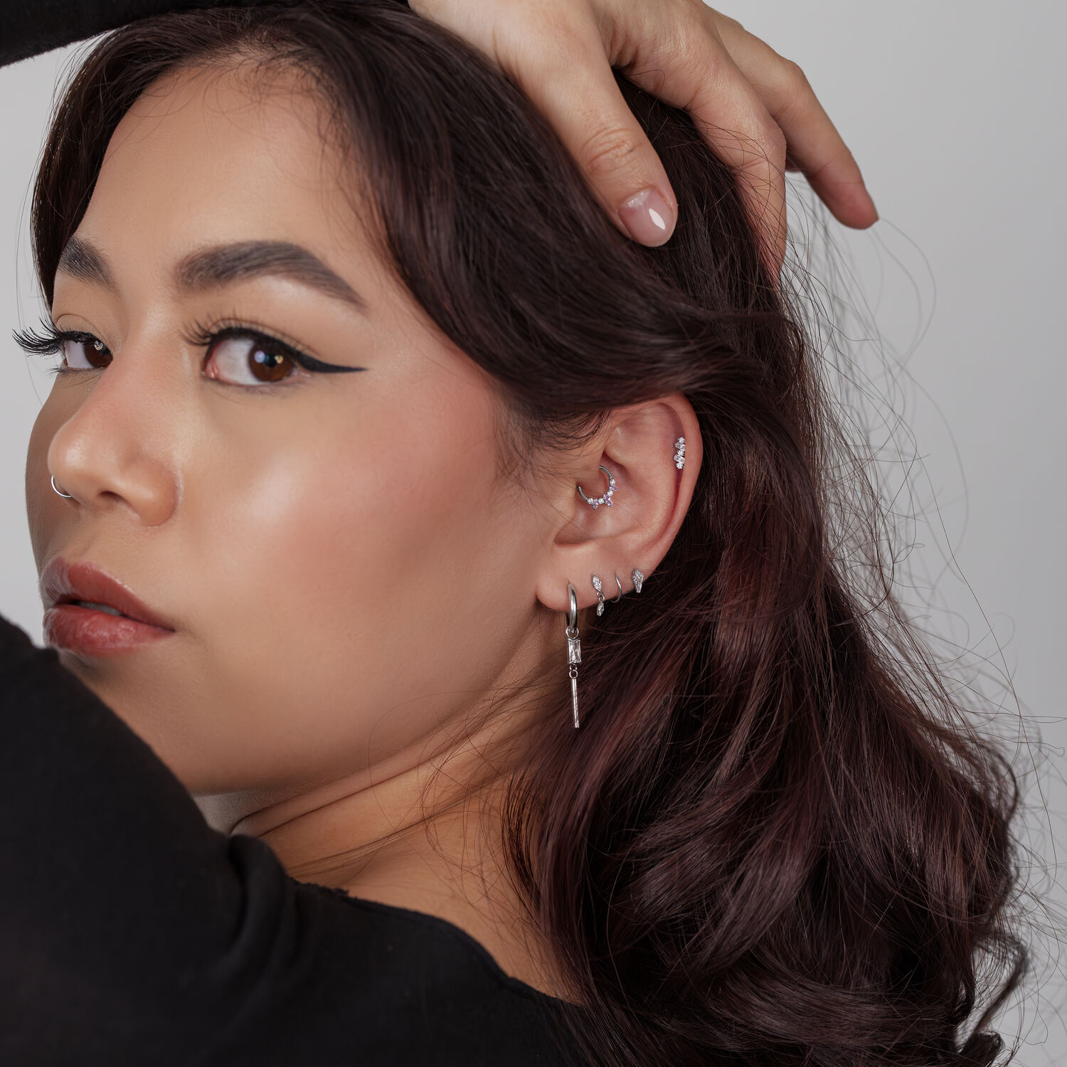 Femme avec plusieurs piercings d'oreille argentés, y compris un embout en cristal, sur fond gris