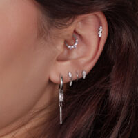 Gros plan d'une oreille avec plusieurs piercings en argent, certains ornés de cristaux