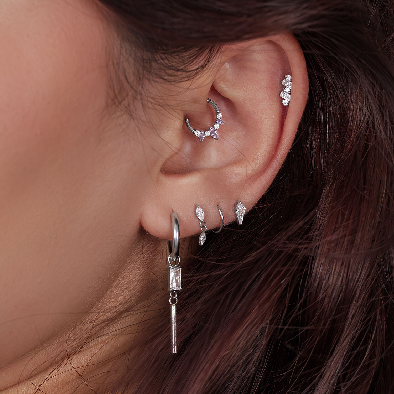 Gros plan d'une oreille avec plusieurs piercings en argent, certains ornés de cristaux