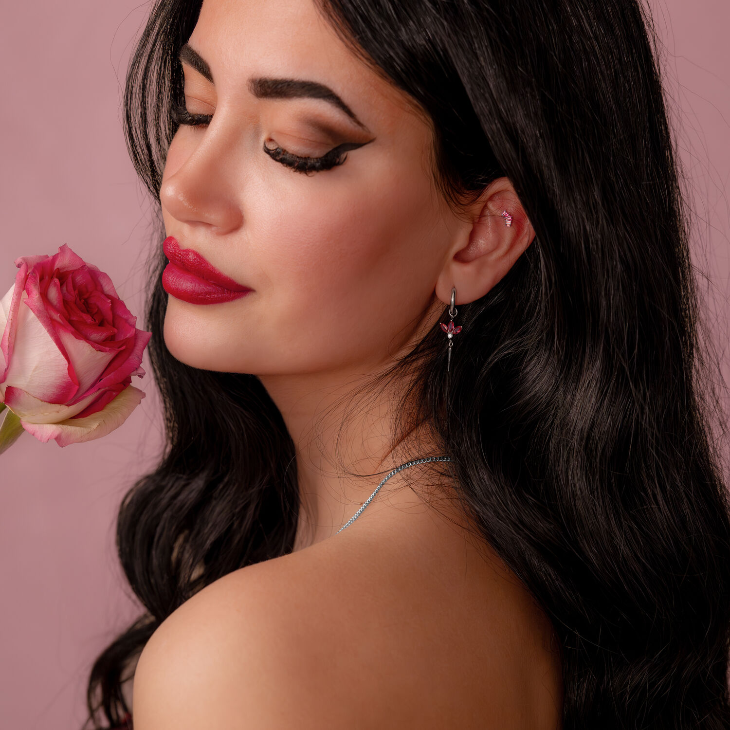 Embout Push Fit argenté avec cristal rouge Femme aux longs cheveux noirs tenant une rose rose et portant une boucle d'oreille argentée avec cristal rouge sur fond rose