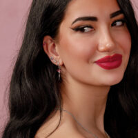 Boucle d'oreille en argent avec pendentif rubis Femme aux longs cheveux noirs portant une boucle d'oreille en argent avec rubis rouge sur fond rose