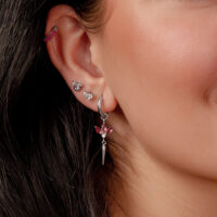 Boucles d'oreilles argentées avec cristaux rouges Gros plan d'une oreille avec plusieurs boucles d'oreilles argentées et cristaux rouges, cheveux foncés en arrière-plan