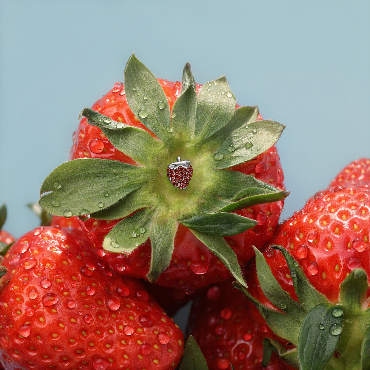Embout fraise en titane pour piercings Embout fraise argenté sur une fraise rouge avec des gouttes d'eau sur fond bleu.