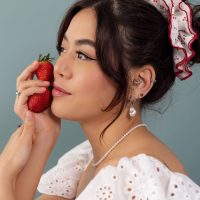 Femme avec fraise et bijoux Femme en robe en dentelle blanche, fraise à la main et boucles d'oreilles devant un fond bleu