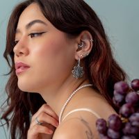Embout Grape Push Fit Argenté Femme avec plusieurs piercings en argent à l'oreille, portant un collier de perles et tenant des raisins.