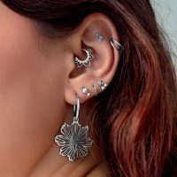 Piercings d'oreille en argent avec pendentif fleur Gros plan d'une oreille avec plusieurs piercings en argent, dont un grand pendentif fleur, sur fond clair