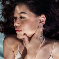 Piercing d'oreille avec embout tortue argenté Femme avec plusieurs piercings d'oreille argentés, dont un embout tortue, sur fond gris