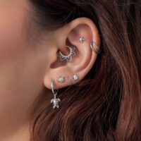 Embouts de piercing d'oreille Tortue argentés Gros plan d'une oreille avec plusieurs embouts de piercing argentés, dont un motif Tortue, sur des cheveux bruns.