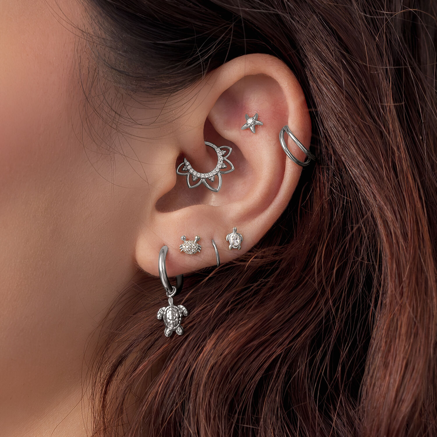 Embouts de piercing d'oreille Tortue argentés Gros plan d'une oreille avec plusieurs embouts de piercing argentés, dont un motif Tortue, sur des cheveux bruns.