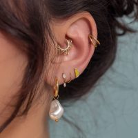 Piercings d'oreille en or avec pendentif perle Gros plan d'une oreille avec plusieurs piercings en or, y compris un pendentif perle, sur fond bleu clair